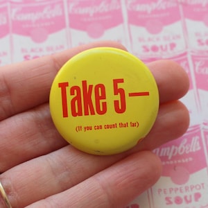 May include: A yellow button with the text "Take 5-" in red, with the phrase "(If you can count that far)" below. The button is held in a hand, with a pink background featuring a repeating pattern of Campbell's soup cans.