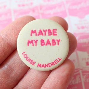 May include: A white button with pink text that reads "MAYBE MY BABY" and "LOUISE MANDRELL".