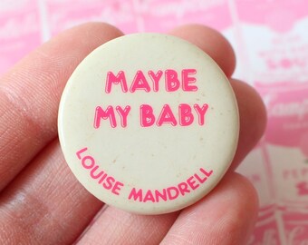 May include: A white button with pink text that reads "MAYBE MY BABY" and "LOUISE MANDRELL".