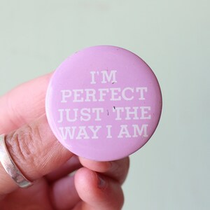 May include: A pink button with the text "I'm perfect just the way I am" in white lettering.