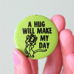 May include: A green button with a black cartoon character and the text "A hug will make my day".