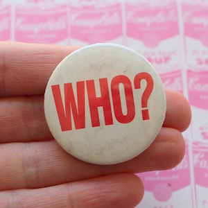 May include: A white button with the words "WHO?" printed in red letters.