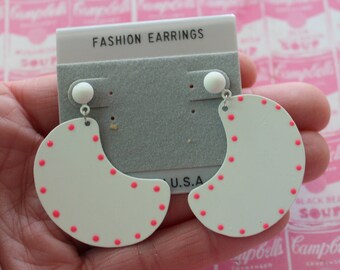 May include: A pair of white and pink half-moon earrings with pink polka dots. The earrings are on a card that says "Fashion Earrings" and "U.S.A."