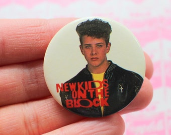 May include: A white button with a red and black image of a young man with the text "New Kids On The Block" printed on it.