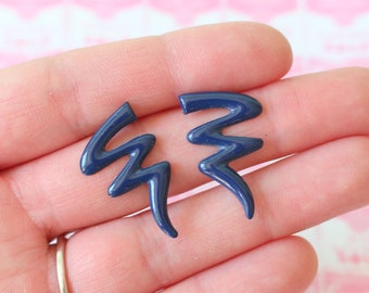 Puede incluir: Un par de pendientes en forma de rayo azul. Los pendientes están hechos de un material liso y brillante.