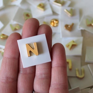 May include: A gold letter N pin on a white card. The pin is surrounded by other letter pins on white cards.