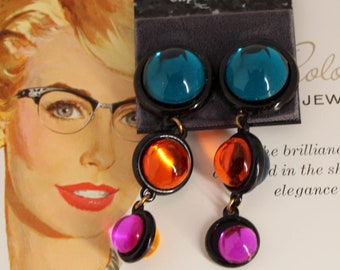 May include: A pair of clip-on earrings with turquoise, orange, and pink glass stones. The earrings are on a white background with the text "Polorama Jewel-Lite" and "Art-Craft".