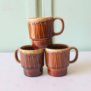 May include: Set of three brown ceramic mugs with a geometric pattern. The mugs are stacked on top of each other.