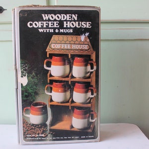 May include: A box for a wooden coffee house with six mugs. The box is brown with a picture of the coffee house and mugs on the front. The text on the box reads "Wooden Coffee House with 6 Mugs" and "Coffee House".