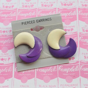 May include: A pair of pierced earrings with a crescent moon design. The earrings are made of purple and white plastic.