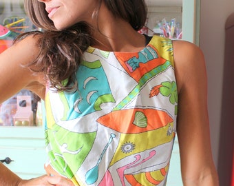 May include: A woman wearing a sleeveless dress with a colorful geometric pattern. The dress has a white background with bright green, blue, orange, and pink shapes. The woman is standing in front of a vintage red refrigerator with flower decals.