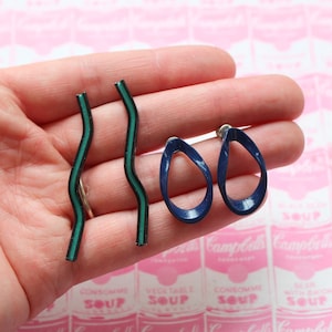 May include: A pair of blue and green earrings. The blue earrings are shaped like a teardrop with a curved line in the center. The green earrings are long and thin with a wavy shape.