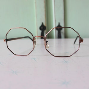 May include: A pair of octagon-shaped glasses with a copper-colored metal frame.
