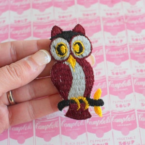 May include: A maroon owl embroidered patch with white and yellow details. The owl is perched on a branch with yellow leaves.