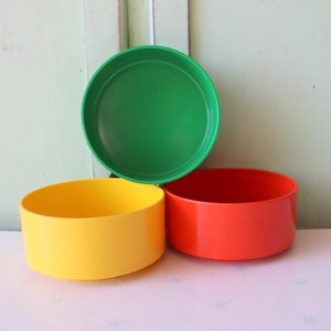 Puede incluir: Tres cuencos redondos de plástico, uno verde, uno amarillo y uno rojo.