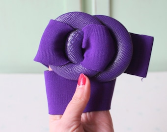 May include: A purple fabric flower with a textured center. The flower is tied with a purple ribbon.