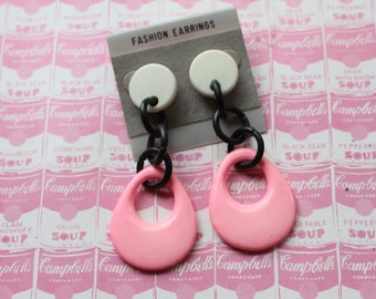 May include: A pair of pink and black dangle earrings with a white circle at the top. The earrings are on a card that says "Fashion Earrings".