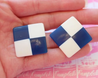 May include: A pair of blue and white checkerboard patterned earrings. The earrings are square shaped and made of plastic.