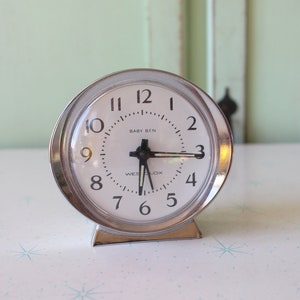 Peut inclure: Un réveil argenté avec un cadran blanc et des aiguilles noires. L'horloge indique "BABY BEN" et "WESTCLOX".