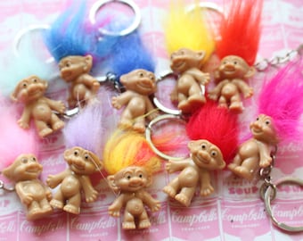 May include: A collection of nine troll doll keychains with colorful fuzzy hair. The keychains are made of plastic and have a troll doll design with a smiling face. The keychains are attached to silver key rings.
