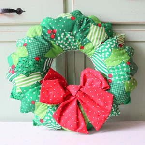 May include: A green and red Christmas wreath made of fabric with a red bow in the center.