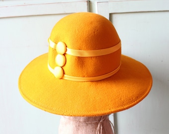 May include: A wide-brimmed yellow felt hat with a yellow ribbon and three yellow buttons.