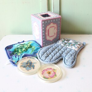 Könnte beinhalten: Ein Set aus vier blauen und weißen bestickten Artikeln, darunter ein Topflappen, zwei Untersetzer und ein Taschentuchbox-Bezug. Die Untersetzer haben Blumenmuster, während der Topflappen ein Blumenmuster und der Taschentuchbox-Bezug einen Buchstaben C hat.