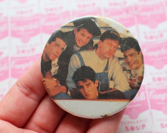 May include: A round button featuring a black and white photo of five young men. The men are wearing casual clothing and smiling. The button is white with a black border.