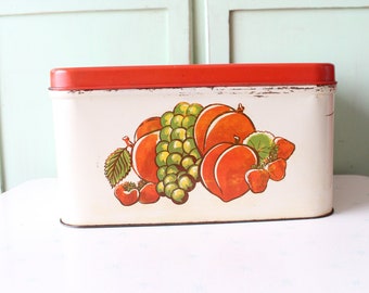 May include: A vintage white metal bread box with a red lid. The front of the box features a colorful illustration of peaches, grapes, and strawberries.
