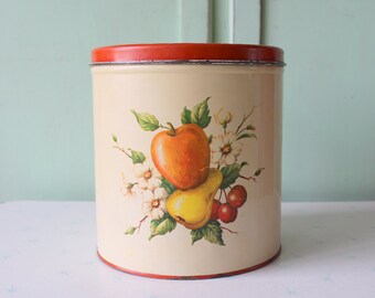 May include: A vintage cream-colored metal canister with a red lid. The canister has a painted design of an apple, pear, and cherries with white flowers.