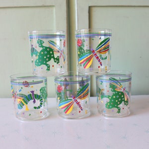 May include: Set of five clear glass tumblers with colorful cartoon designs. Each glass features a different design of a frog, a dragonfly, and confetti.