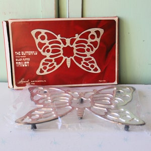 Puede incluir: Un salvamanteles de mariposa plateado en su embalaje original. La caja es roja con letras blancas que dicen "The Butterfly, Handcrafted, Silver Plated Trivet".