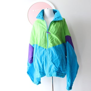 May include: A retro colour-blocked jacket in bright shades of green, blue, and purple. The jacket has a zip-up front, a high collar, and long sleeves. The jacket is displayed on a mannequin.