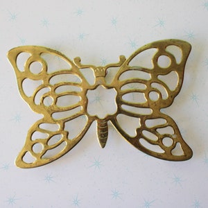 Puede incluir: Un posa-platos de metal dorado en forma de mariposa con un diseño recortado.