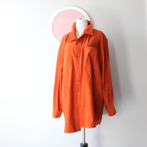 Könnte beinhalten: Ein langärmeliges orangefarbenes Wildledershirt mit Knopfleiste und einer einzigen Tasche auf der linken Brust.