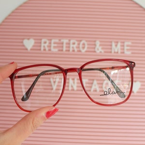 May include: Red plastic framed eyeglasses with clear lenses. The brand name "elan" is printed on the right lens.