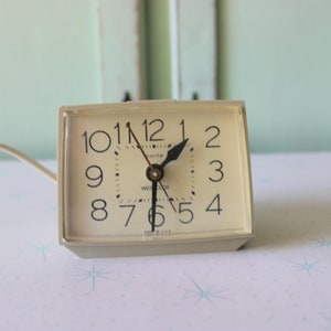 Puede incluir: Un reloj despertador analógico blanco con números y manecillas negros. La esfera del reloj indica "10 11 12 1 2 3 4 5 6 7 8 9" y tiene la palabra "Westclox" impresa.