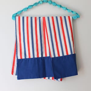 May include: Two red, white, and blue striped pillowcases with blue hems hanging on a turquoise beaded hanger.