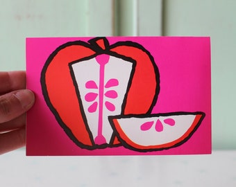 May include: A pink card with a red and white apple illustration. The apple is cut in half, revealing the inside with pink seeds. A slice of apple is next to the whole apple.