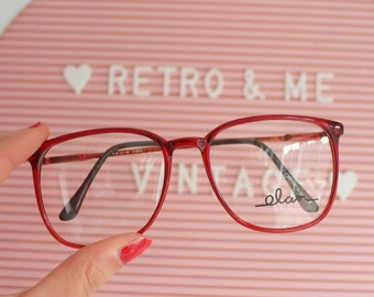 Könnte beinhalten: Rote Kunststoff-Brille mit klaren Gläsern. Der Markenname "elan" ist auf dem rechten Glas aufgedruckt.