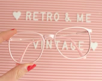 May include: Pink round glasses with a clear lens. The glasses are held in front of a pink letter board with the words "Retro & Me Vintage" on it.