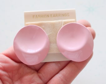 May include: A pair of pink plastic clip-on earrings. The earrings are round and have a slight curve to them. The earrings are on a white card that says "Fashion Earrings".