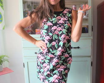 May include: A sleeveless black dress with a pink flamingo print. The dress has a scoop neck and a relaxed fit.