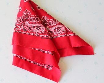 Puede incluir: Un pañuelo rojo con un patrón paisley en blanco y negro. El pañuelo está doblado por la mitad y tiene un borde blanco.