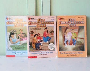 May include: Three paperback books from The Baby-Sitters Club series. The books are titled "Claudia and the Red Joke", "Claudia and the Genius of Elm Street", and "The Ghost at Dawn's House".