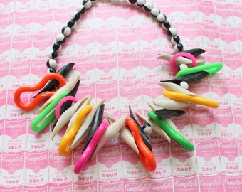Könnte beinhalten: Eine bunte Halskette aus Plastik und schwarz-weißen Perlen. Die Halskette hat verschiedene Formen und Farben, darunter Orange, Pink, Grün und Weiß.