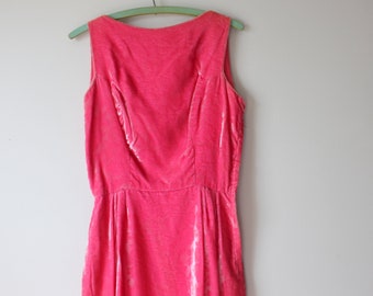 May include: A sleeveless, vintage-style dress in a vibrant pink hue. The dress is made of a soft, textured fabric, possibly velvet, and hangs from a green wooden hanger. The dress features a fitted bodice and a gently flared skirt.