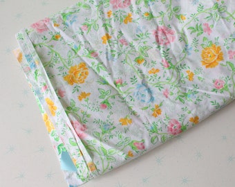 Puede incluir: Una tela blanca con un patrón floral con flores rosas, amarillas y azules sobre enredaderas verdes. La tela tiene un ribete azul claro.