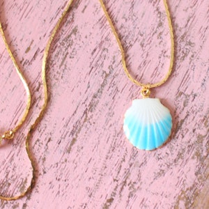 May include: A gold chain necklace with a blue and white seashell pendant.