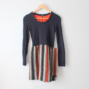 May include: A navy blue long-sleeved dress with a geometric patterned skirt in black, white and orange.